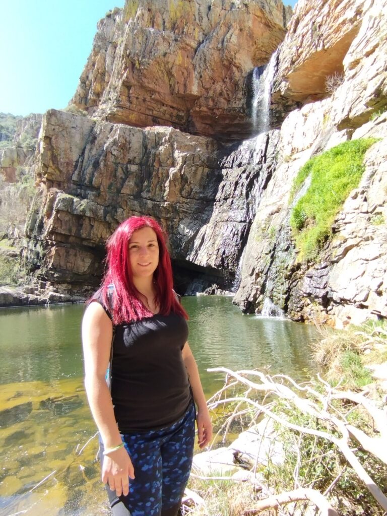 Mujer con el pelo rojo junto a una laguna con cascada en la Cascada de la Cimbarra