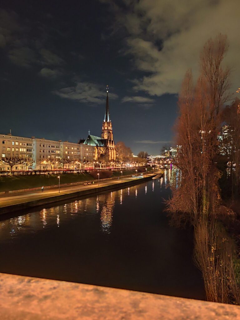Vista nocturna de Frankfurt con una iglesia iluminada y reflejada en el río Meno